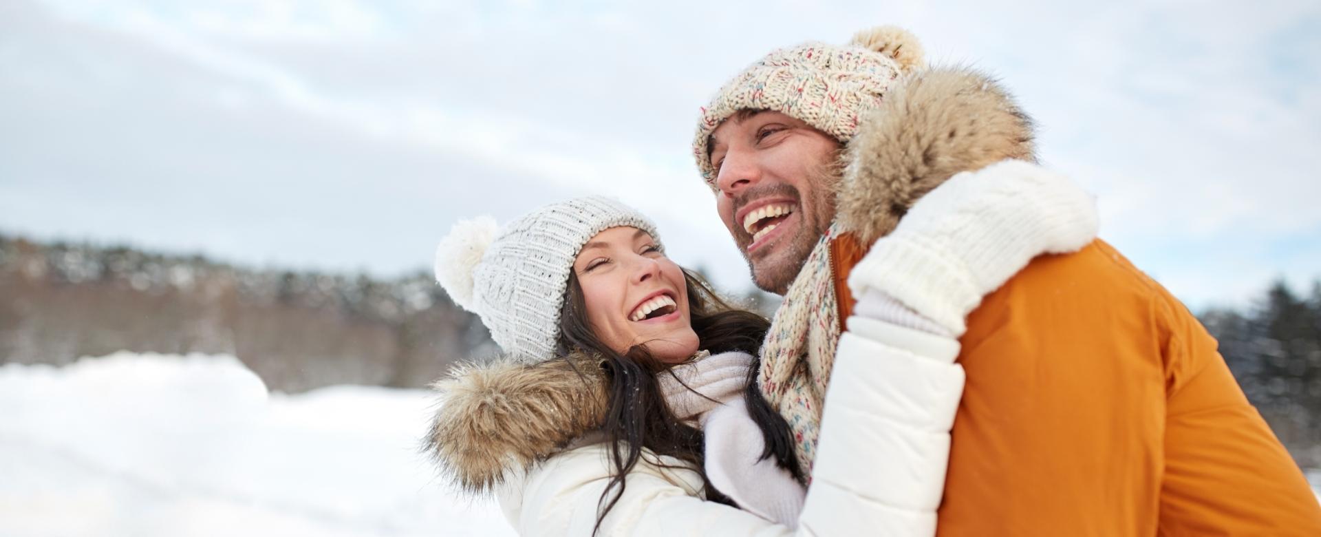 Coppia felice abbracciata sulla neve, sorridente e vestita con abiti invernali.