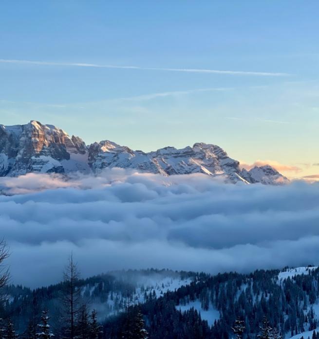 Snowy mountains above the clouds with a sunset sky.